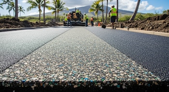 Obreros construyen un camino con una máquina pavimentadora en Hawái, bajo palmeras. Primer plano de un corte de pavimento con material oscuro y granulado de colores.