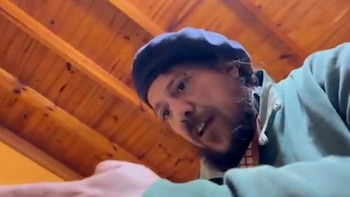 Un hombre con boina y barba mira hacia abajo frente a la cámara en un espacio con techo de madera