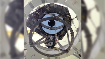 Estructura interna de un telescopio con armazón metálico, cableado, componentes electrónicos, una apertura circular al cielo y el logo de Airbus