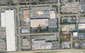 Imagen satelital de un área urbana industrial en Miami, mostrando grandes edificios, almacenes, estacionamientos, vehículos y una red de calles principales