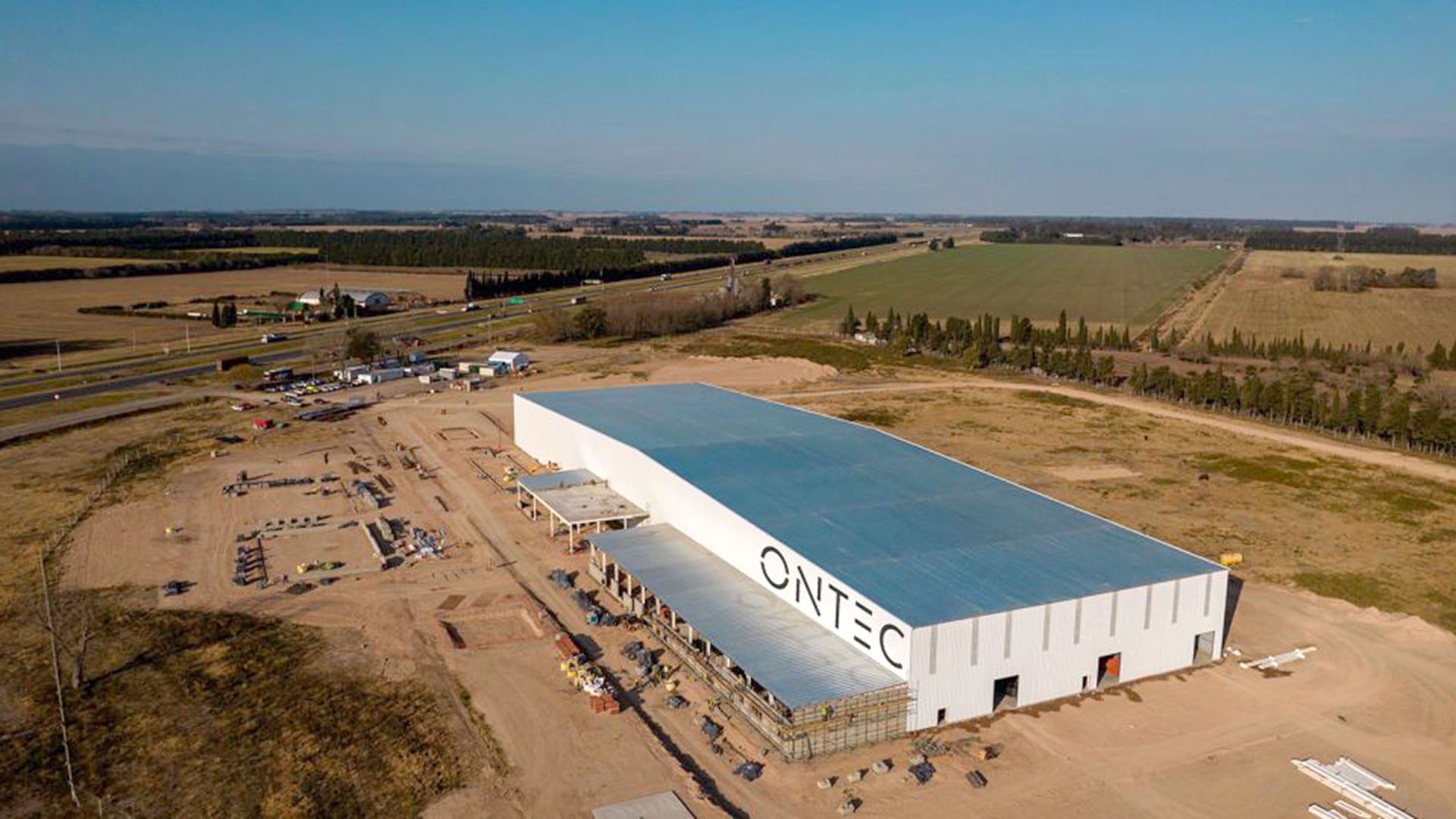 Vista aérea de la planta ONTEC de Mirgor en Baradero, dedicada a la producción de autopartes, mostrando su avance de construcción con infraestructura vial y campos aledaños. (mirgor.com)