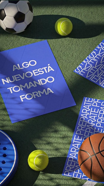 Balón de fútbol, dos pelotas de tenis, una paleta de pádel, un balón de baloncesto y tres carteles azules con texto blanco sobre superficie verde