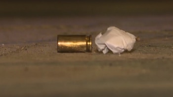 Un casquillo de bala dorado y un trozo de papel blanco arrugado sobre una superficie de cemento rugosa y oscura