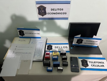 Una mesa con documentos, sellos, laptop negra y teléfono móvil negro. Letreros categorizan "Documentación", "Sellos", "Elementos Informáticos", "Telefonía Celular"