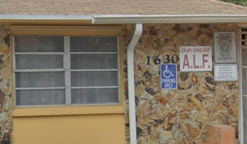 Fachada de edificio con revestimiento de piedra, ventana, canalón, número 1630, letrero 'OUR DREAM A.L.F.' y cartel de estacionamiento con silla de ruedas
