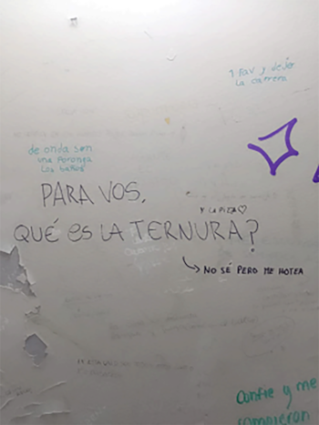 Una pared blanca con múltiples mensajes escritos a mano con marcadores de varios colores. Destaca la frase grande "PARA VOS, QUÉ ES LA TERNURA?" y dibujos