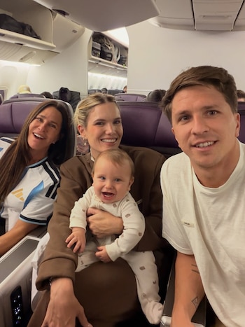 Cuatro personas sonrientes en el interior de un avión: una mujer de cabello oscuro, una rubia sosteniendo un bebé riendo, y un hombre mirando a cámara