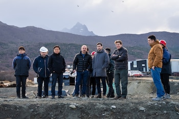 Un grupo de diez personas, incluyendo al gobernador Gustavo Melella, de pie sobre un terreno de tierra. Detrás, montañas y edificios industriales bajo un cielo nublado