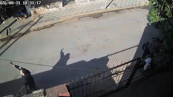 Vista desde una cámara de seguridad hacia una calle asfaltada con personas y sombras junto a una reja metálica