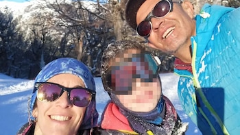 Selfie de tres personas sonriendo en un paisaje nevado; una mujer con bandana azul, un niño con gafas de esquí y un hombre con chaqueta azul