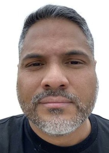 Retrato de frente de un hombre con cabello corto canoso, barba corta y camiseta negra sobre fondo blanco