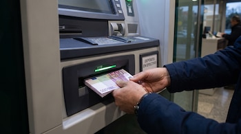 Manos de una persona que introducen un fajo de billetes de 500 euros en la ranura de depósito de un cajero automático.