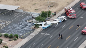 Vista aérea de un avión pequeño blanco y azul en una calle urbana. Líneas eléctricas caídas, vehículos de emergencia, personal de policía y bomberos