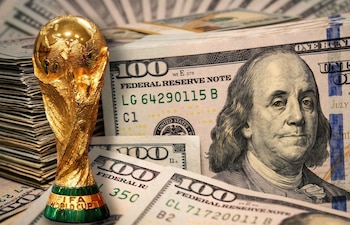 Una Copa Mundial de la FIFA dorada sobre pilas de billetes de cien dólares estadounidenses, con el retrato de Benjamin Franklin visible en primer plano