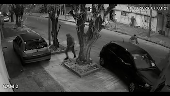 Imagen en blanco y negro de una cámara de seguridad con dos automóviles estacionados y personas caminando por la acera