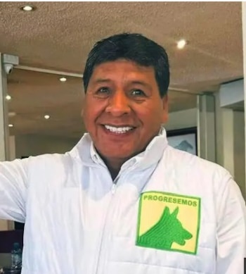 Un hombre sonríe vistiendo una chaqueta blanca con un parche verde que muestra la palabra Progresemos y el dibujo de un perro