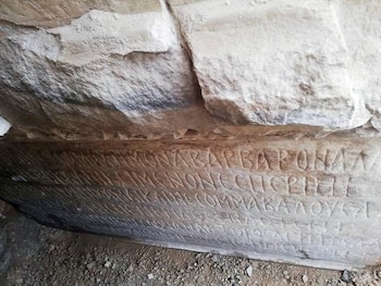 Una imagen cercana muestra una antigua inscripción tallada en una superficie rocosa, con varias líneas de caracteres visibles y la textura de la piedra irregular
