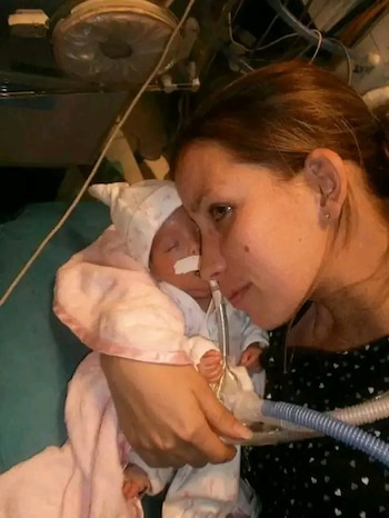 Analia Boutet sostiene a su bebé prematuro, envuelto en una manta rosa, con un tubo respiratorio en su nariz. Analia lo mira con ternura en un hospital