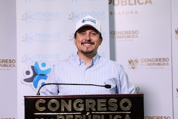 Hombre con gorra blanca y camisa a cuadros azul y blanco sonríe detrás de un podio con el texto 'CONGRESO DE LA REPÚBLICA' y el logo de Moot en el fondo