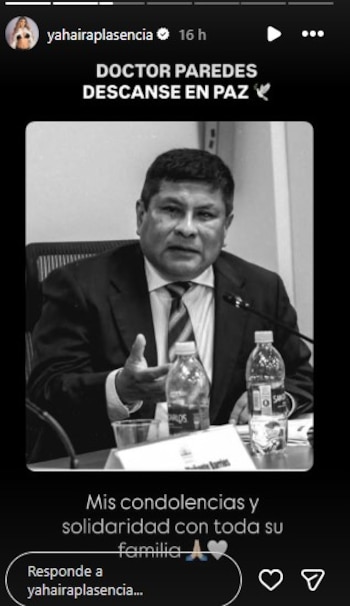 Fotografía en blanco y negro de un hombre de mediana edad, vestido con traje y corbata a rayas, sentado en una mesa con dos botellas de agua