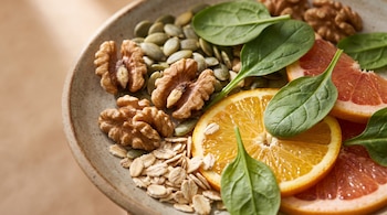Plato con nueces, semillas de calabaza, avena, rodajas de naranja, rodajas de pomelo y hojas de espinaca.
