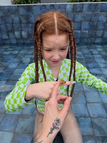 Niña pelirroja con trenzas en una piscina, una mariposa se posa en su dedo índice mientras otra mano la señala