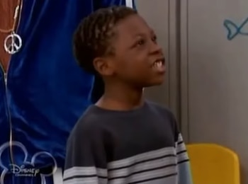 Un niño afroamericano con una camiseta de manga larga a rayas habla en una habitación junto al logotipo de Disney Channel