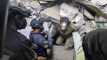 Tres rescatistas con cascos, linternas frontales, guantes y mascarillas trabajan entre bloques de concreto y escombros de una estructura derrumbada