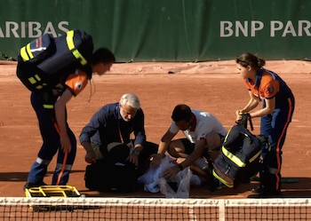 Jakub Mensik yace en una cancha de tenis de arcilla siendo asistido por personal médico y un oficial. Se ve una red de tenis y un letrero "BNP Paribas" al fondo