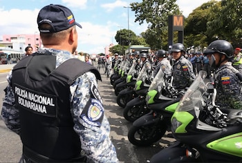 Un oficial de la Policía Nacional Bolivariana visto de espaldas, con un chaleco y gorra, frente a una fila de policías uniformados sobre motocicletas en Caracas
