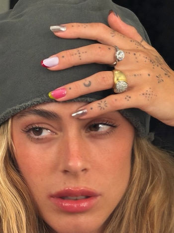 Un primer plano de la mano de Stoessel mostró sus anillos dorados y de plata, las uñas multicolor y los tatuajes de puntos que cubren el dorso
