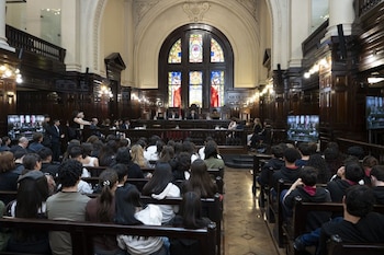 alumnos en bancos de madera frente a un estrado judicial, pantallas de video y un vitral en una sala con paredes de madera