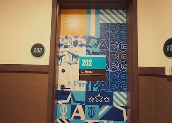 Una puerta de hotel decorada con los colores celeste y blanco de Argentina, con un cartel que indica "202 L. Messi" y el número "202" en la pared