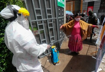 Un miembro del Sistema Departamental de Salud desinfecta a una mujer en la entrada del coliseo Julio Borelli en La Paz (Bolivia). EFE/ Martín Alipaz/Archivo