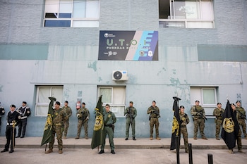 Agentes policiales con uniformes camuflados y banderas se alinean frente a una fachada con el cartel de UTOI en San Isidro