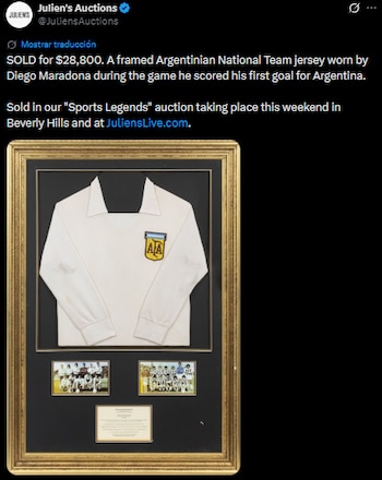 Una camiseta blanca de manga larga de la selección argentina enmarcada, con el escudo del equipo. Debajo, dos pequeñas fotos de equipo y una placa informativa