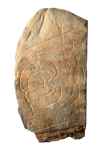 Estela de piedra de tonos ocre con grabados. Se observan formas circulares, líneas rectas y figuras esquemáticas