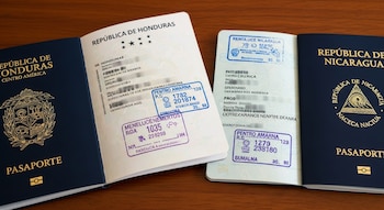 Dos pasaportes abiertos, uno de Honduras y otro de Nicaragua, con sus páginas interiores visibles, sellos de aduanas y texto personal borroso.