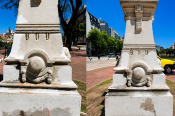 Base de escultura de piedra blanca con detalles decorativos y manchas por deterioro, dividida en dos vistas, con árboles, edificios y personas al fondo