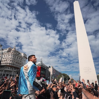 Un hombre con la bandera argentina sobre los hombros es alzado por una multitud festiva que graba con teléfonos móviles, con el Obelisco de Buenos Aires y edificios al fondo