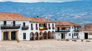 Carretera asfaltada y mojada con señalización vial, rodeada de laderas verdes, árboles y una casa en una zona rural montañosa