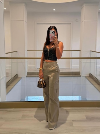 Antonela Roccuzzo de pie en un pasillo moderno con paredes blancas, pilares y barandillas de cristal, tomándose una selfie en un espejo
