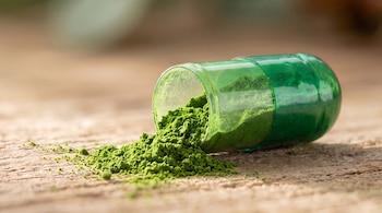 Cápsula verde abierta en una superficie de madera, con polvo verde en su interior y un montículo de polvo fuera.