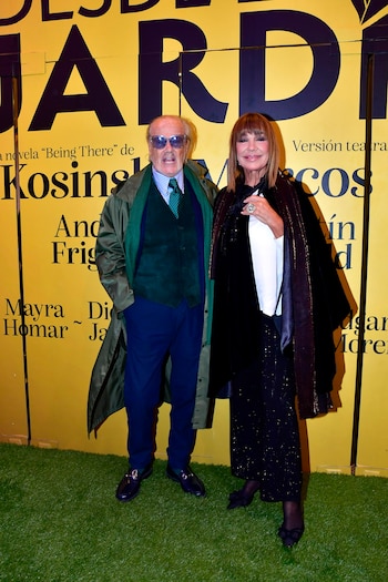 Un hombre y una mujer sonrientes posan de pie frente a un telón amarillo con el título "DESDE EL JARDÍN" y un suelo de césped artificial verde