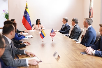 Personas vestidas formalmente se sientan alrededor de una mesa con pequeñas banderas de Venezuela y Estados Unidos