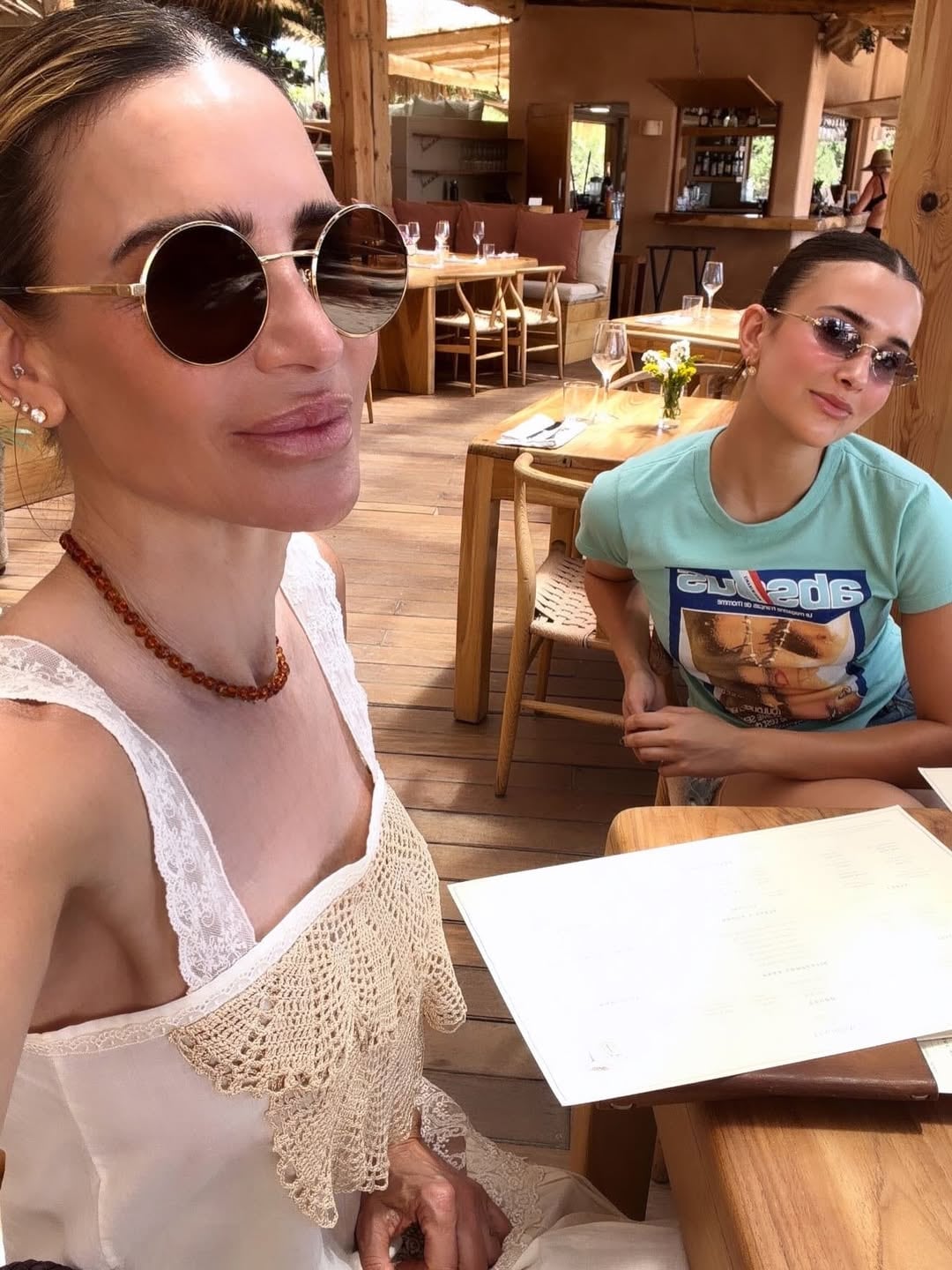 María Vázquez con su hija en el beach club, con el vestido blanco de crochet y collar de ámbar