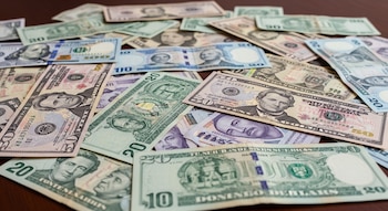 Vista de cerca de varios billetes esparcidos, incluyendo dólares estadounidenses, quetzales guatemaltecos, lempiras hondureñas y pesos dominicanos.