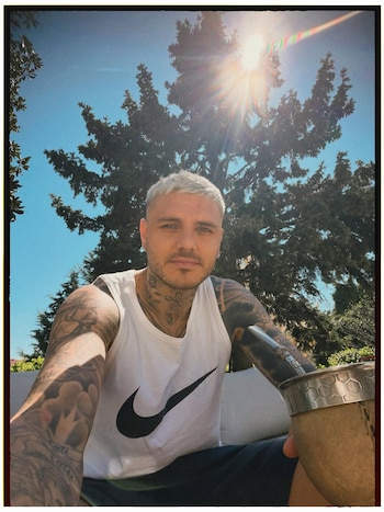 Primer plano de Mauro Icardi con pelo rubio y tatuajes, vistiendo una camiseta sin mangas Nike, bebiendo mate al aire libre bajo el sol