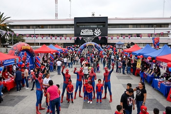 Personas con disfraces del Hombre Araña posan en una explanada con carpas rojas y azules frente al edificio de la alcaldía Gustavo A. Madero