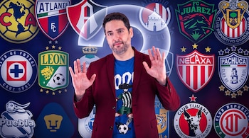Hombre con barba, blazer y camiseta de futbolista, manos levantadas, rodeado de numerosos escudos de clubes de fútbol y un signo de interrogación luminoso.